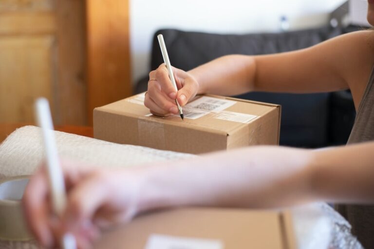 Two people write labels on boxes to make a parcel.