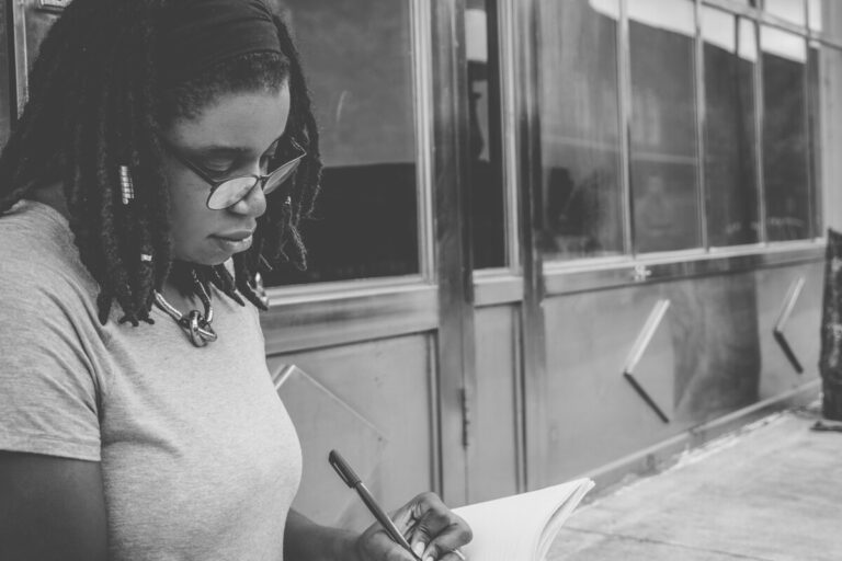 Black woman sitting at a desk writing. Photo: Unsplash.com