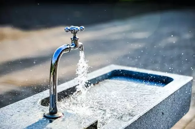 Water flowers into a sink or trough from a short pipe and tap, in the open air in the sunshine.