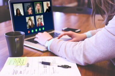 Woman on video conference on a laptop, with a mug, pen and paper on the desk