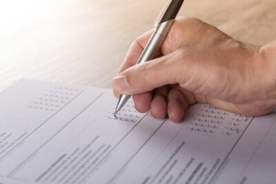 Man's hand holding a pen, completing a survey by Andreas Breitling from Pixabay