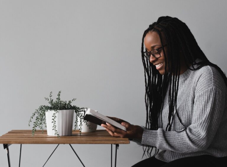 A black woman with long hair and glasses reading at a small table