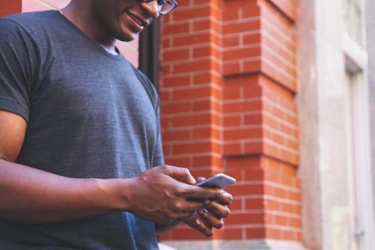 a man in a t-shirt by a red brick wall texting