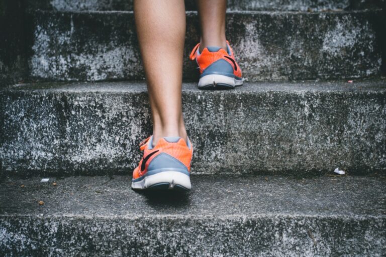 the back of a woman's legs and orange & grey trainers as she heads up a flight of concrete stairs