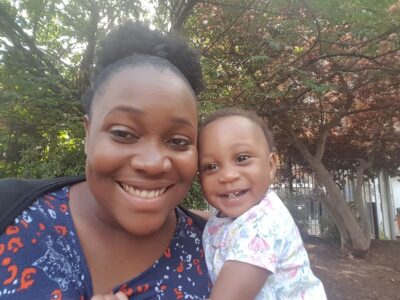 A woman smiles at the camera, holding her baby