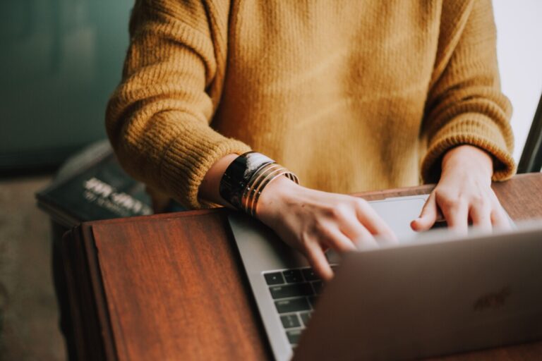 A woman in a dark yellow jumper and bangles working at a laptop