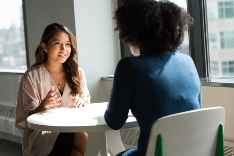 Two businesswoman talk over a small white table