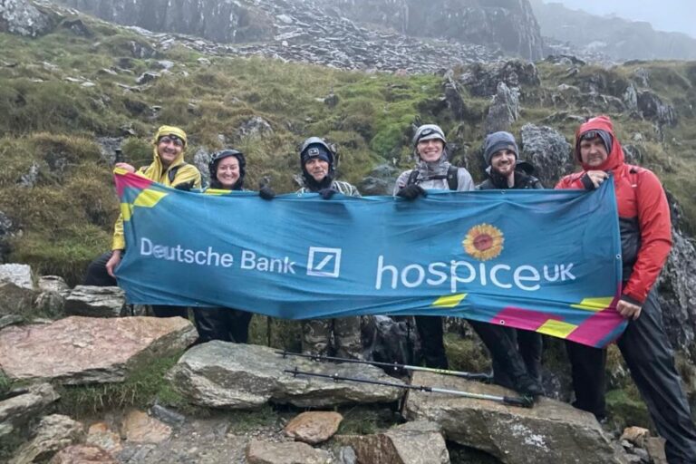 deutsche-bank-employees hold up a hospice uk banner on a rainy rocky hillside