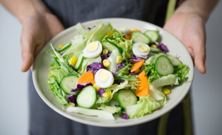 hands holding a plate full of a mixed salad including eggs lettuce cucumber and carrot