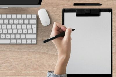 a hand holds a pen over a clipboard, poised to write