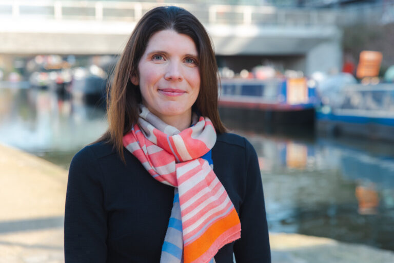 Sarah Vibert, CEO of the NCVO faces the camera in a black coat and colourful scarf