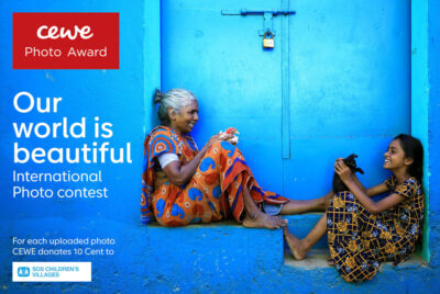 CEWE Photo Award promotion - "our world is beautiful", featuring two women on steps outside a blue house walls, steps and doors. Photo: Udayan Sankar Pal