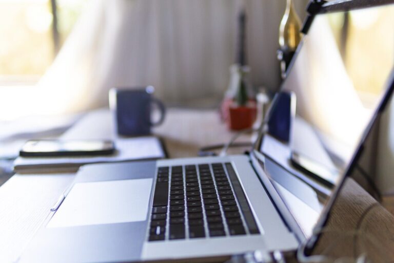 An open laptop sits in the foreground with a coffee, phone and notepad just visible at the back. By Joshua Woroniecki from Pixabay