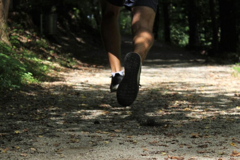 A man runs through the dappled light of woodland. By Tara Glaser on Unsplash