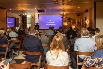 An audience faces a speaker and a screen that says Cynozure