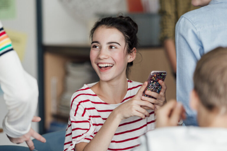 Student teenage girl laughing and talking while in class, using phone.