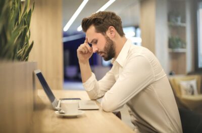 A man sits at his laptop with head in hand. Photo by Andrea Piacquadio on pexels