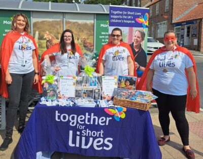 Morrisons employees dressed in red caps stand behind a stall being held for Together for Short Lives