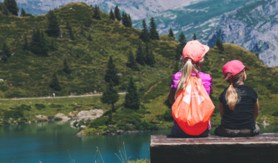 Two young girls in baseball caps and with a backpack sit on a bench gazing out at mountains. From the Pawprint Trust