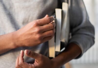 hands carrying a pile of books under an arm