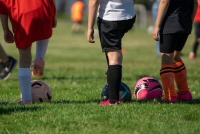 A low shot of 3 kids in football gear, each with a football. By Joshua Choate on Pixabay