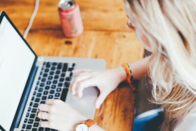 A woman on a laptop, with a can of drink by her side on a wooden table