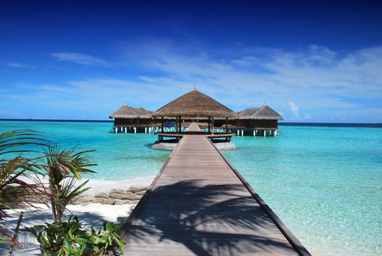 a deck leading out to huts in a blue sea. By Pixabay on Pexels