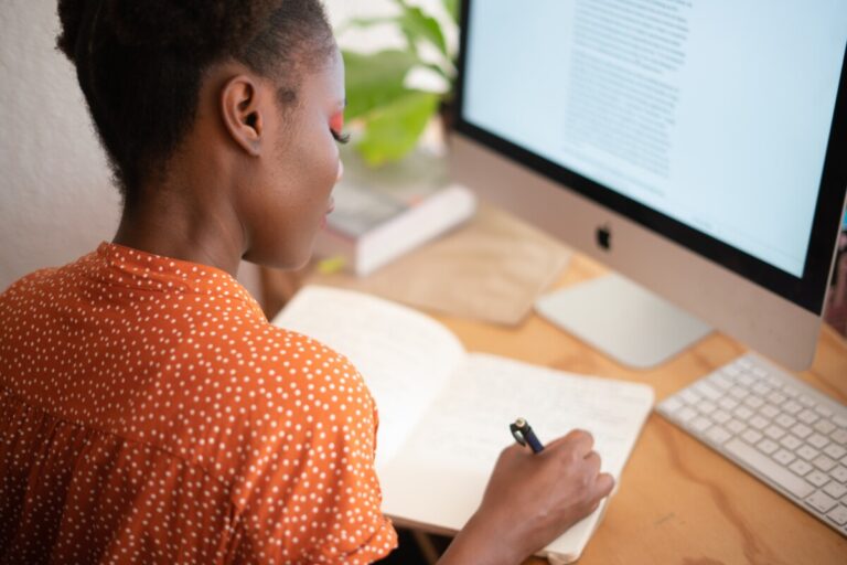 A woman writes in a notebook in front of her computer. By R F Studio on Pexels