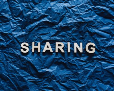 Capital letters spell "SHARING" on a wrinkled blue paper background. Photo: Pexels.com