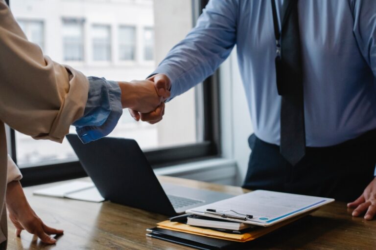 A man and woman shake hands over a desk. By Sora Shimazaki