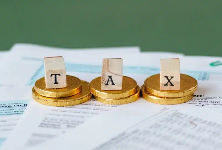 Wooden blocks spelling out tax sit on top of gold coins. By Nataliya Vaitkevich on Pexels