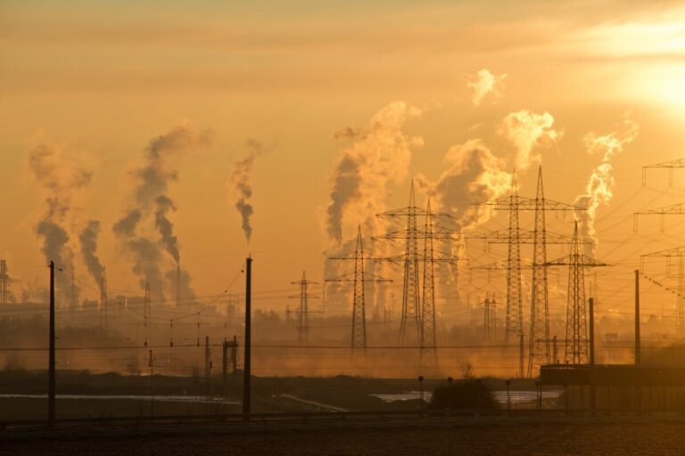 Pylons and chimneys smoking against a sunset sky. By Pixabay on pexels