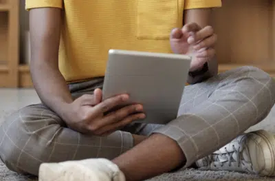 A teen boy sits cross legged on the floor, holding a tablet. By Julia Cameron on Pixabay