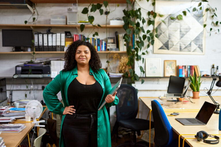 A mixed race middle-aged woman stands in an office, with her hand on her hip