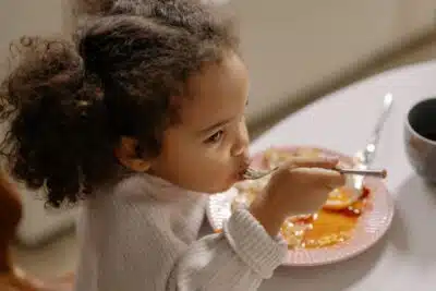 A young girl with bunches eats with a spoon. By Cottonbro studio on pexels