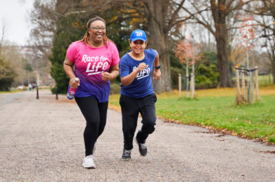 A mum and her child run, wearing big smiles and CRUK Race for Life t-shirts