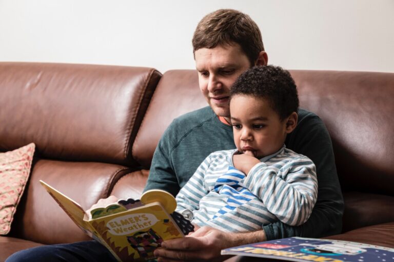 A dad reads a story to his young son who is sitting on his lap
