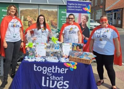 Morrisons employees dressed in red caps stand behind a stall being held for Together for Short Lives