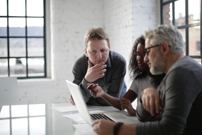 three people in a white office space look at a computer. By Andrea Piacquadio on pexels