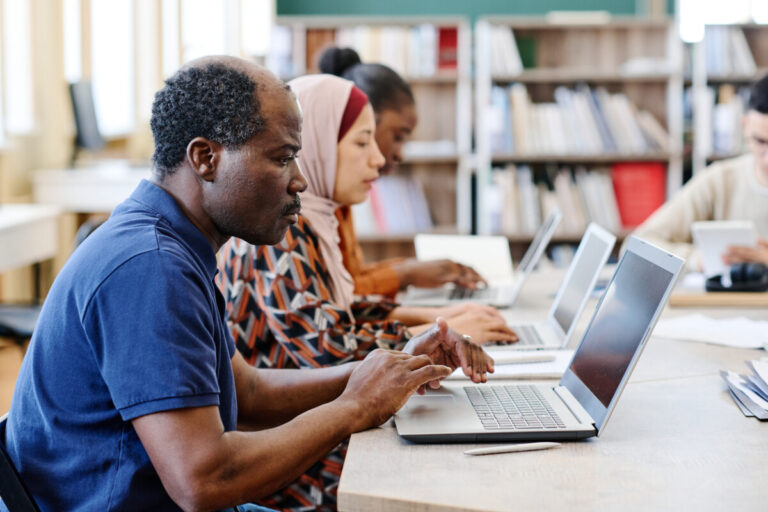 Group of ethnically diverse immigrant students working on laptops during lesson searching for information on the Internet