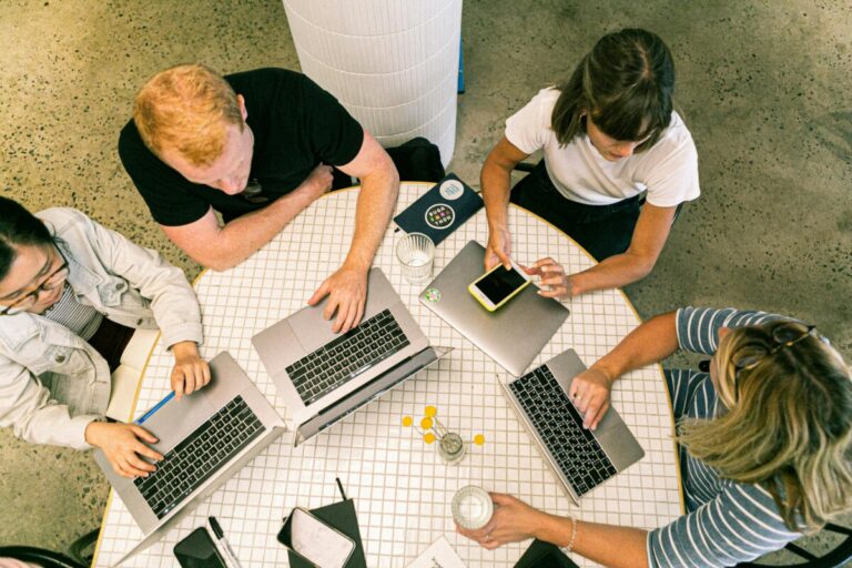 A shot from above looking at a group of people sitting around a table with laptops. By Canva Studio.