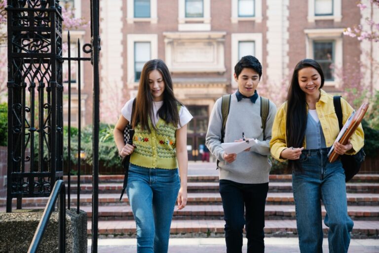 Three university students walk towards the camera, talking and smiling. By George Pak on Pexels