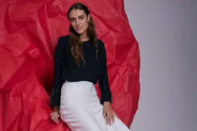 A woman in a black shirt and white skirt sits against a red background as part of Salvation Army's Take Back Scheme fashion campaign, encouraging people to donate more unwanted clothing