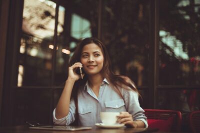 A young woman on her phone, with a coffee. By chevanon on Pexels