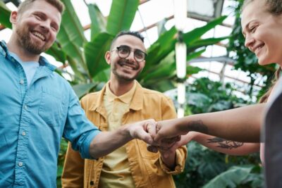 a group of people smil as they fistbump, surrounded by plants. By Fauxels on pexels