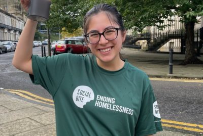 A woman smiles in a green Social Bite 100 Mile Challenge t-shirt