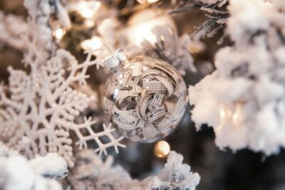 A bauble filled with pieces of paper showing musical notes, on a white Christmas tree. By Ryan Johns on Unsplash