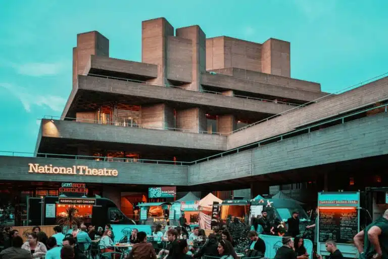 A picture of the National Theatre in London as the sun sets on a summer evening, with people sitting outside enjoying a drink. By Samuel Regan Asante on unsplash