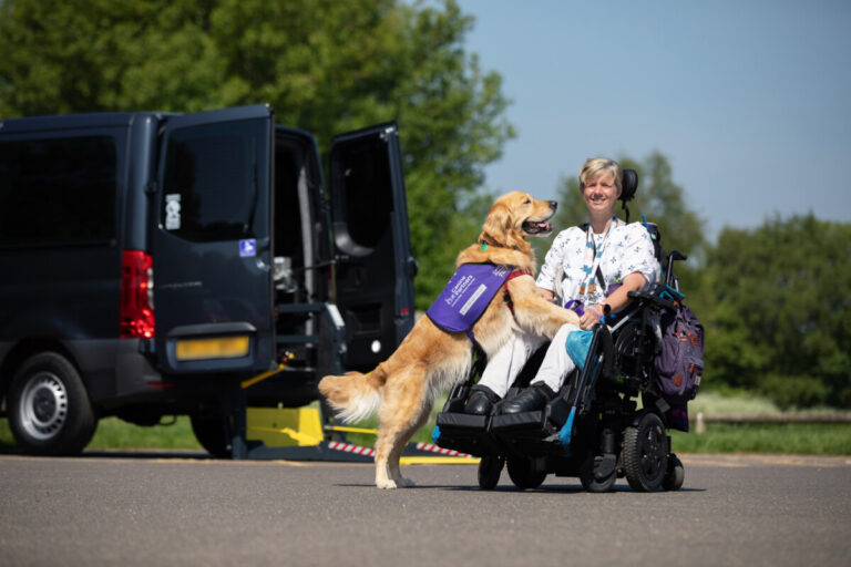 Samantha in a wheelchair with her Hearing Dog next to a Motability vehicle.