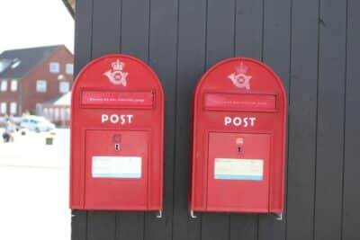 Two red Danish postboxes side by side on a wooden building in the snow.
